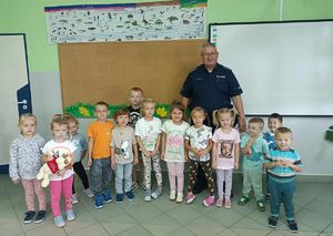 Dzielnicowi stoi z przedszkolakami w sali.