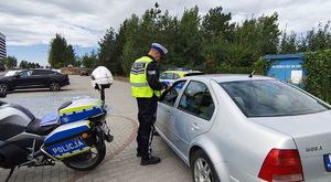Policjant stoi r przy zatrzymanym do kontroli dorgowej pojazdem.