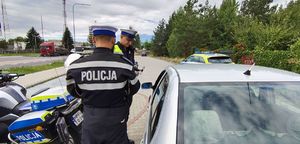 Policjanci stoją przy zatrzymanym do kontroli pojazdem.