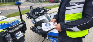 Policjant trzyma w ręku ulotki akcji mistrzu zwolnij.