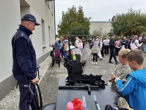 Policjant prezentuje dzieciom elementy umundurowania policyjnego na pikniku.