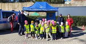 Stoisko profilaktyczne pod namiotem, policjantka rozmawia z dziećmi. obok stoi radiowóz.