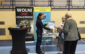 Policjantka na stoisku profilaktycznym w hali WOSiR rozmawia z seniorami.