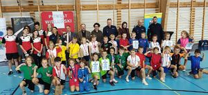 Zaproszeni goście, uczniowie oraz nauczyciele, laureaci z pucharami, nagrodami i dyplomami w hali sportowej stoją obok siebie.