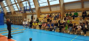 Hala sportowa. Policjantka stoi przed dziećmi i opiekunami , którzy siedzą na trybunach.
