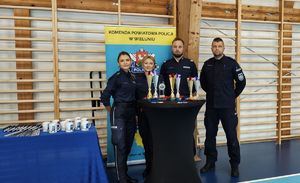 Hala sportowa. Stolik na którym ustawione są puchary, medale. Za stolikiem stoją policjanci.