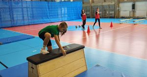 Hala sportowa. Dziewczynka przeskakuje przez skrzynię do ćwiczeń na torze przeszkód.