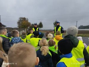 Policjanci, obok dzieci ubrane w kamizelki odblaskowe.