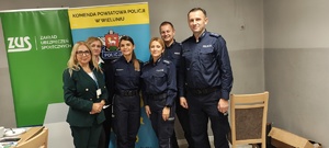 Policjanci i przedstawicielki ZUS stoją przy rolapach w sali ośrodka.