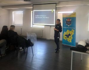Policjantka w sali z  użyciem prezentacji prowadzi prelekcje z uczniami.