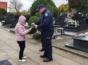 Dzielnicowi wręczają elementy odblaskowe i ulotki na cmentarzu przechodniom.