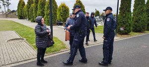 Dzielnicowi wręczają elementy odblaskowe i ulotki na cmentarzu przechodniom.