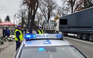 Radiowóz  i policjanci nadzorują ruch przy cmentarzu.
