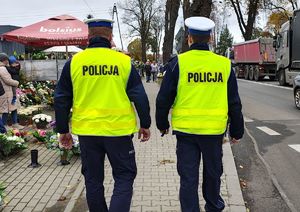 Policjanci idą po chodniku wzdłuż drogi przy cmentarzu.