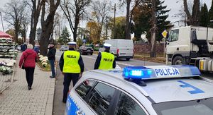 Radiowóz  i policjanci nadzorują ruch przy cmentarzu.