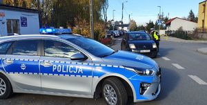 Radiowóz, w tle policjantka stoi przy pojeździe, który się zatrzymał.