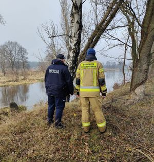 Policjant i strażak stoją przy rzece.