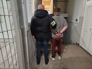 Policjant prowadzi zatrzymanego po korytarzu w budynku komendy.