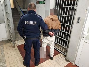 Policjant prowadzi zatrzymanego po korytarzu w budynku komendy.