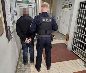 Policjant prowadzi zatrzymanego po korytarzu w budynku komendy.