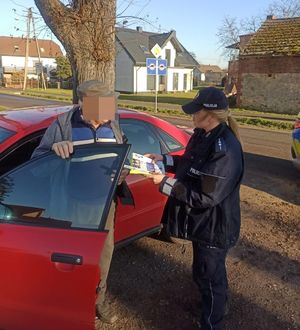 Policjantka wręcza mężczyźnie stojącemu przy samochodzie ulotki.