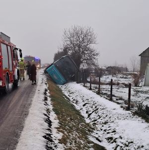 Wóz strażacki stojący na drodze, wokół strażacy oraz autobus częściowo przechylony w rowie.