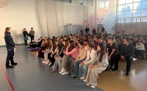 Policjantka prowadzi prelekcję w sali gimnastycznej gdzie dzieci siedzą na ławkach.