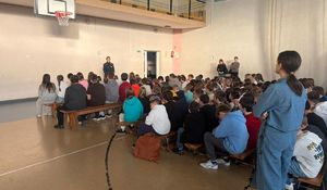 Policjantka prowadzi prelekcję w sali gimnastycznej gdzie dzieci siedzą na ławkach.