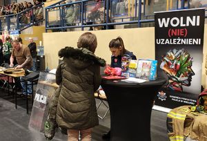 Policjantka na stoisku profilaktyczny stoi przy stole, na przeciwko niej stoi kobieta.