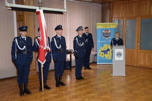 W auli wieluńskiej jednostki Policji podczas uroczystej zbiórki stoi poczet sztandarowy, dowódca uroczystości oraz lektor przy mównicy.