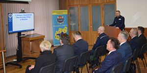 Uczestnicy  narady rocznej siedzą na krzesłach w sali odpraw, przy mównicy stoi I Zastępca Komendant Powiatowy Policji w Wieluniu.