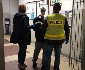 Policjanci prowadzą zatrzymanego po korytarzu w budynku komendy.