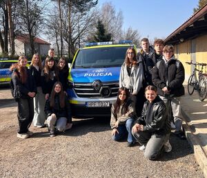 Radiowóz policyjny, policjant oraz młodzież zgromadzona wokół niego.