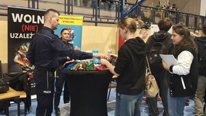 Hala Wieluńskiego Ośrodka Sportu i Rekreacji , uczestnicy targów edukacji przy stoisku rozmawiają z policjantami.