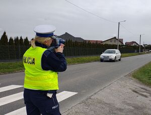 Policjanci stoją przy radiowozie, jeden trzyma w  ręku miernik prędkości.