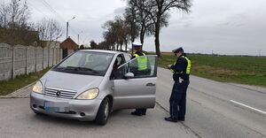 Policjanci stoją przy radiowozie, jeden trzyma w  ręku miernik prędkości.
