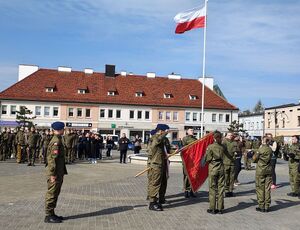 Plac Legionów w Wieluniu,  uczniowie klas wojskowych w mundurach stoją w pododdziałach, maszt z flagą państwową, zaproszeni goście w trakcie uroczystości ślubowania