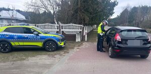 Policjant prowadzi kontrolę pojazdu, z boku stoi radiowóz.