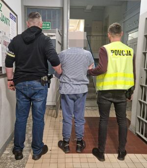 Policjanci prowadzą zatrzymanego po korytarzu.