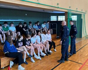 Hala sportowa w Szkole Podstawowej w Osjakowie, młodzież siedzi na ławkach, policjanci stoją przed nimi.