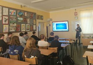 Policjantka w sali lekcyjnej prowadzi pogadankę z uczniami, którzy siedzą w ławkach.