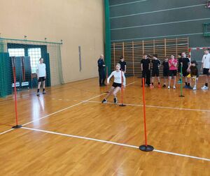 Hala sportowa w Szkole Podstawowej w Osjakowie, młodzież stoi wokół sali wspólnie z policjantami, jedna z dziewczyn biegnie pomiędzy przeszkodami.