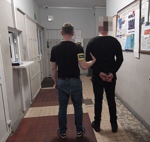 Policjant prowadzi zatrzymanego po korytarzu w budynku komendy.