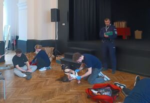 Sala Wieluńskiego Domu Kultury, uczniowie w ramach rywalizacji prowadzą praktyczne zadania z zakresu udzielania pierwszej pomocy. W sali obecny również policjant.