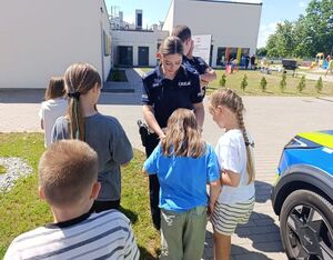 Policjantka wręcza dzieciom elementy odblaskowe.