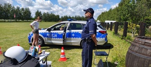 Stoisko profilaktyczne, policjant. W tle radiowóz, w którym siedzi dziecko.