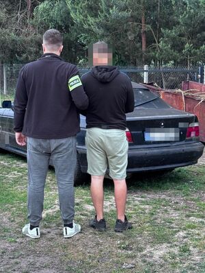 W tle odzyskany przez policjantów samochód BMW oraz policjant, który prowadzi zatrzymanego.