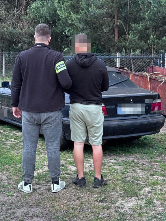 W tle odzyskany przez policjantów samochód BMW oraz policjant, który prowadzi zatrzymanego.