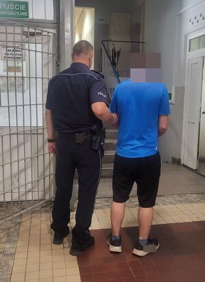 Policjant prowadzi zatrzymanego po korytarzu w budynku komendy.