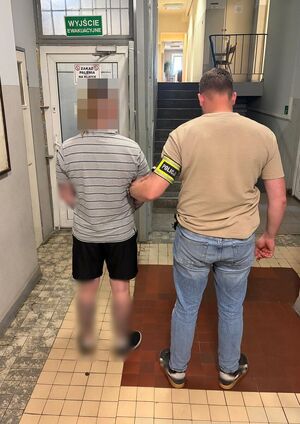 Policjant prowadzi zatrzymanego po korytarzu w budynku komendy.